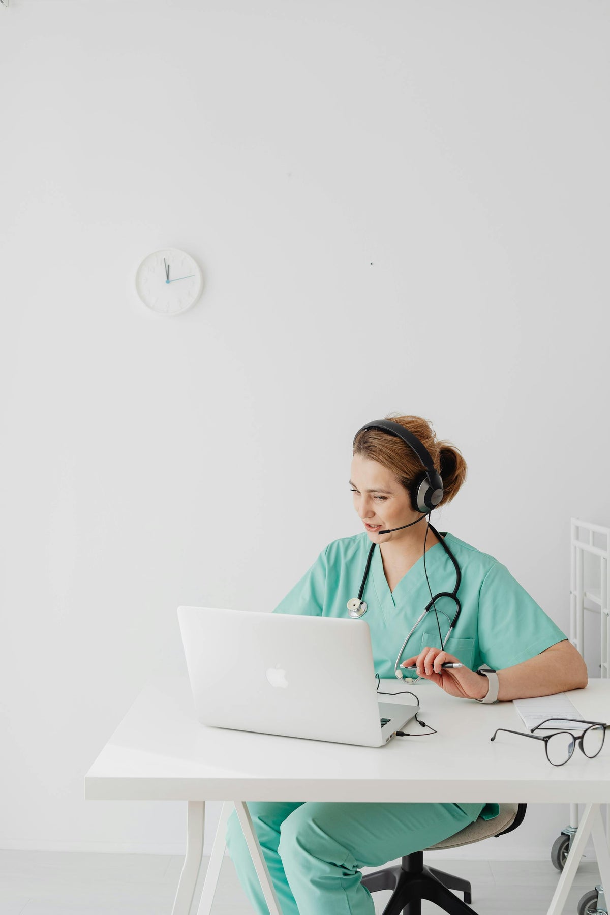 Nurse in scrubs working on a laptop with a headset